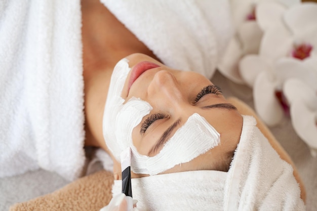 Jong mooi meisje in masker voor het ontspannen van het gezicht in de spa salon