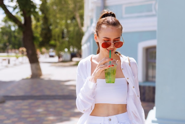 Jong mooi meisje in witte kleren en rode bril drinkt een zomerse verfrissende cocktail