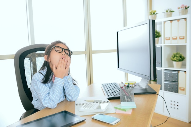 jong mooi meisje kinderen zakelijke werknemer zittend op een computerbureau werken lange tijd moe voelen en geeuwen op kantoor.