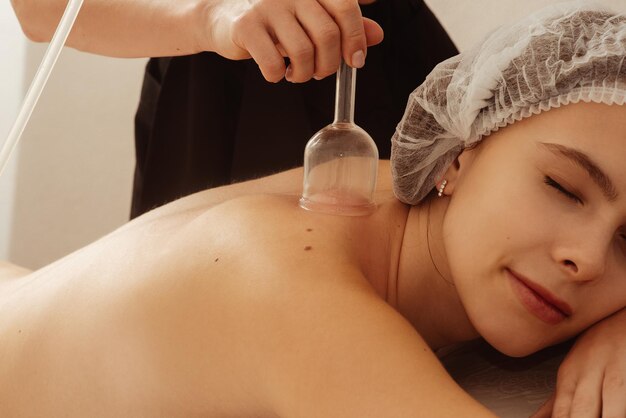 Jong mooi meisje ligt op een bank in een cosmetische hoed met gesloten ogen in een spa salon masseur doet massage procedures