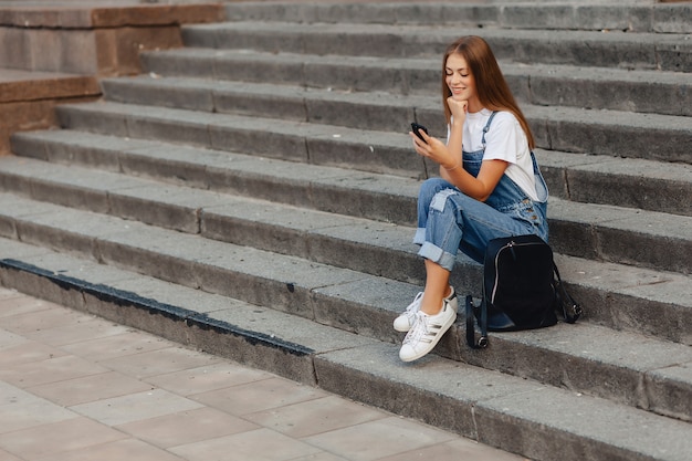 Jong mooi meisje met aktentaszitting op treden en het schrijven van sms op telefoon