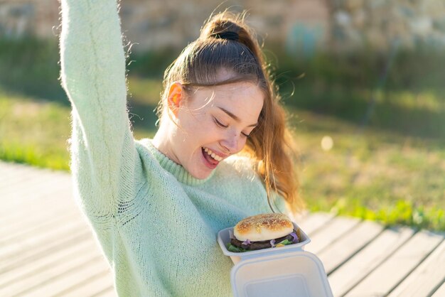 Jong mooi meisje met een hamburger in de open lucht