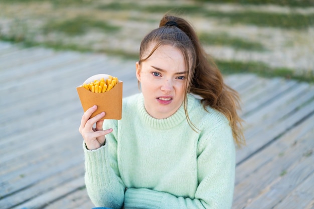 Jong mooi meisje met gebakken chips in de open lucht met droevige uitdrukking