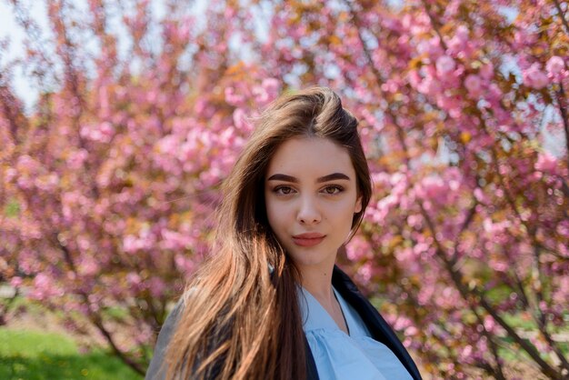 Jong mooi meisje met lang haar geniet van de schoonheid van de lentenatuur in de buurt van de bloeiende sakura
