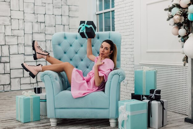 Jong mooi meisje poseren in een roze korte jurk op een turquoise fauteuil met geschenken