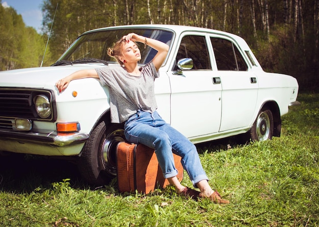 Jong mooi meisje zit naast een oude auto