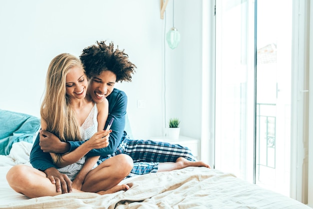 Jong mooi paar tussen verschillende rassen in bed gelukkig met zwangerschapstestxa