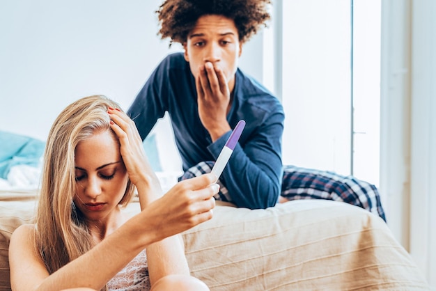 Foto jong mooi paar tussen verschillende rassen in bed ongelukkig met zwangerschap