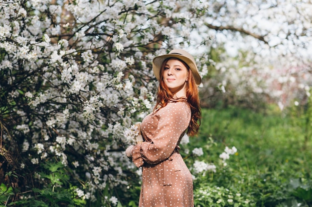 Jong mooi roodharig meisje loopt in een lente bloeiende appelboomgaard