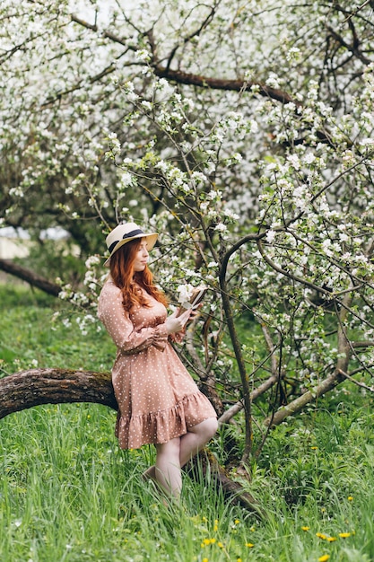 Jong mooi roodharig meisje loopt in een lente bloeiende appelboomgaard