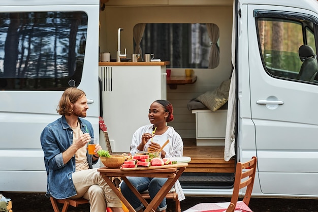 Jong multi-etnisch koppel aan tafel zitten en samen lunchen tijdens picknick in het bos