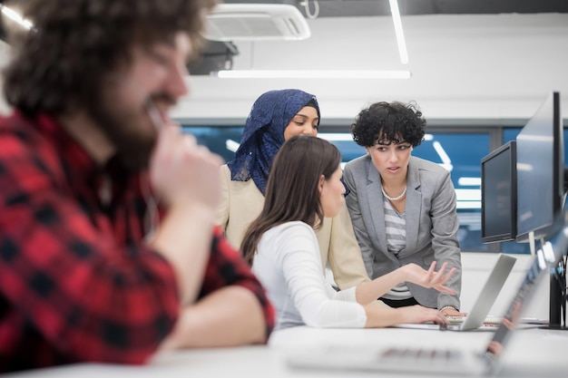 jong multi-etnisch zakelijk team van softwareontwikkelaars die samenwerken met behulp van laptop en desktopcomputer tijdens het schrijven van programmeercode bij modern startup-kantoor