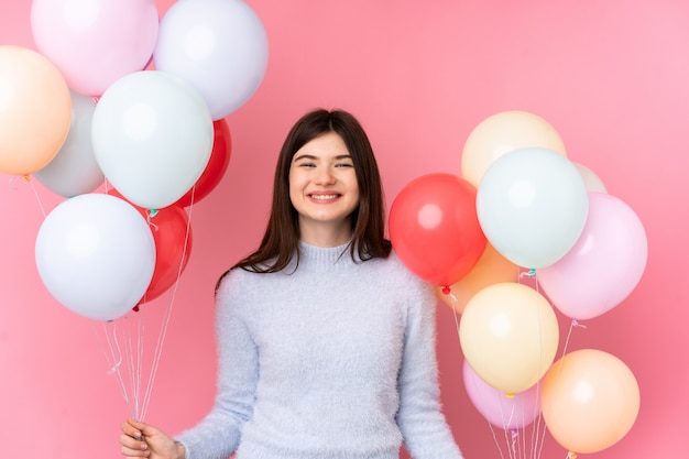 Jong Oekraïens tienermeisje dat veel ballons over geïsoleerde roze muur houdt