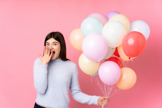 Jong Oekraïens tienermeisje dat veel ballons over roze muur met verraste gelaatsuitdrukking houdt