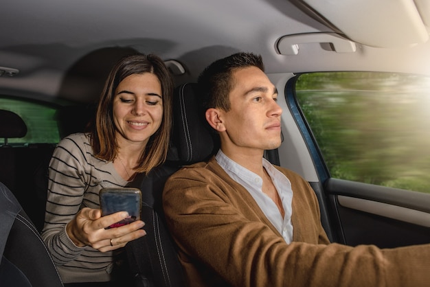 Jong paar in auto. Man rijdt en vrouw lacht tijdens het gebruik van smartphone.