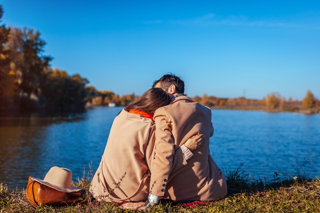 Jong paar in liefde chillen door herfst meer en knuffelen