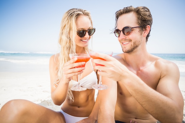 Jong paar in zonnebril die cocktailglas op het strand roosteren