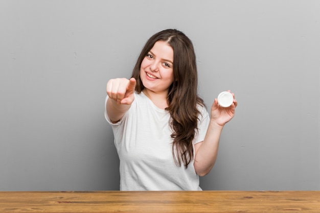 Jong plus size bochtige vrouw met een vochtinbrengende crème vrolijke glimlach wijzend naar voren.