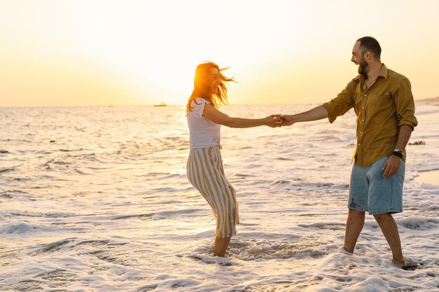 Jong romantisch paar dansen zich omdraaiend door zee Zeegezicht bij zonsondergang met mooie lucht Romantisch paar op het strand bij gouden zonsondergang Minnaar paar plezier op het strand