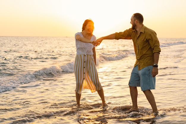 Jong romantisch paar dansen zich omdraaiend door zee Zeegezicht bij zonsondergang met mooie lucht Romantisch paar op het strand bij gouden zonsondergang Minnaar paar plezier op het strand