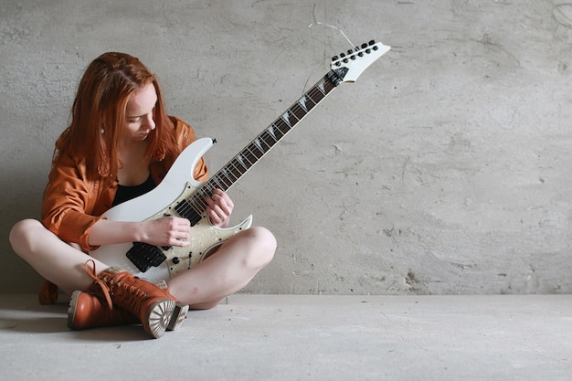 Jong roodharig meisje met elektrische gitaar. Rockmuzikant meisje in een leren jas. Ze is een mooie zangeres en een performer van rockmuziek.