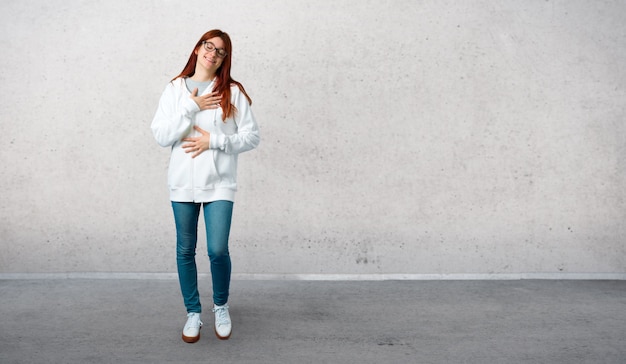 Jong roodharigemeisje in een stedelijk wit sweatshirt met glazen die een partij glimlachen