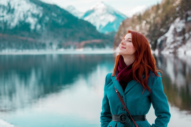 Jong roodharigemeisje in vacht dichtbij meer in Alpen, Duitsland