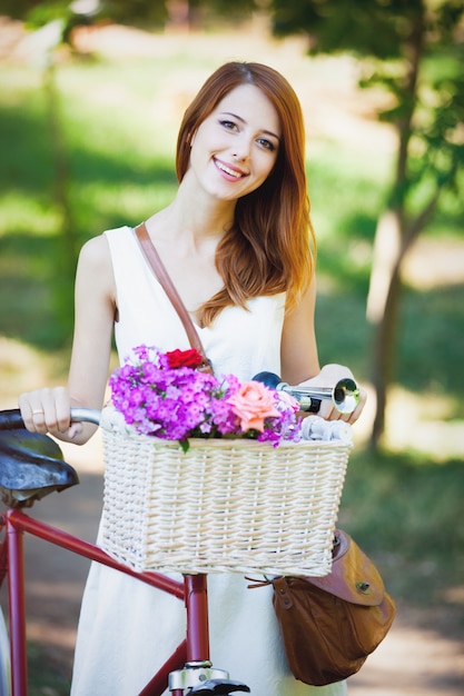 Jong roodharigemeisje met bloemen in fietsmand in de lente openlucht