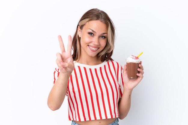 Jong Russisch meisje met cappuccino geïsoleerd op een witte achtergrond glimlachend en overwinningsteken tonen
