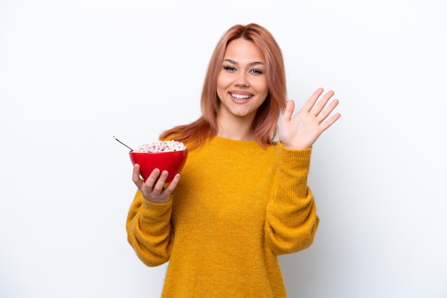 Jong Russisch meisje met een kom cornflakes geïsoleerd op een witte achtergrond saluerend met de hand met gelukkige expressie