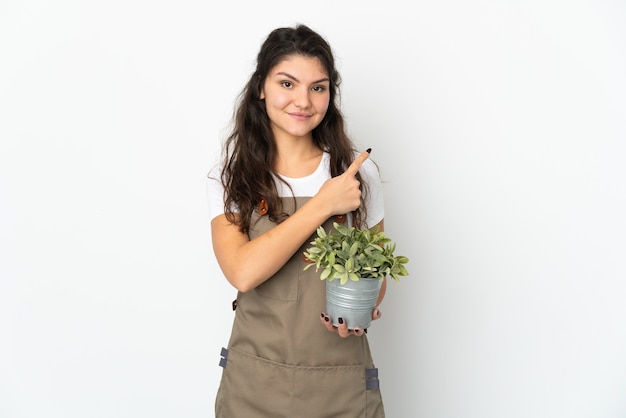 Jong Russisch tuinmanmeisje dat een geïsoleerde plant vasthoudt en naar de zijkant wijst om een product te presenteren