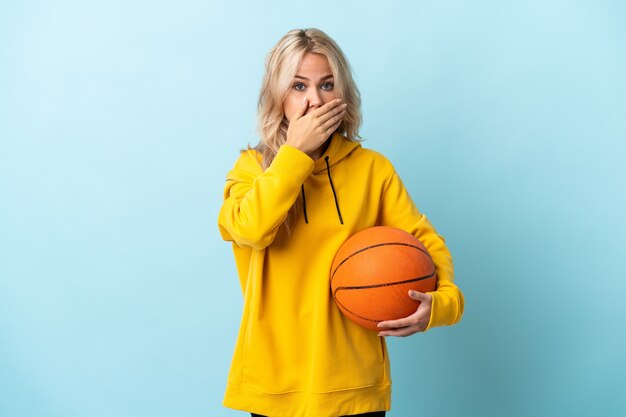 Jong Russisch vrouwen speelbasketbal dat op blauwe achtergrond wordt geïsoleerd die mond behandelt met hand