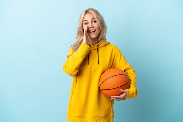 Jong Russisch vrouwen speelbasketbal dat op blauwe muur wordt geïsoleerd die met wijd open mond schreeuwt