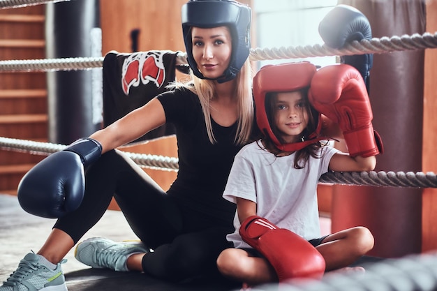 Jong schattig meisje in helm en haar mooie vrouwelijke bokstrainer poseren voor fotograaf op de ring.