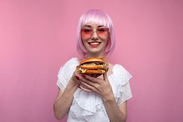 Jong schattig meisje met roze kort haar houdt grote hamburger in haar handen en glimlacht vrouw toont hamburger