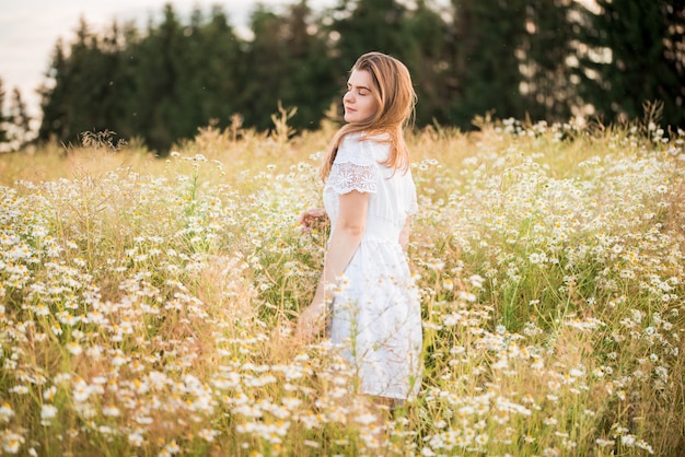 Jong schattig meisje, tedere dromerig verliefd, in een veld met madeliefjes. in jurk en rieten hoed. hete zonnige zomer, zonsondergang in het dorp. vrijheid concept en levensstijl