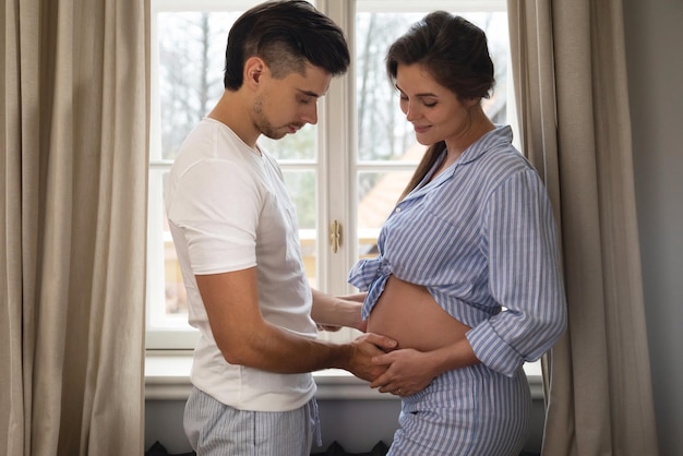 Jong sensueel stel wacht op een baby Man en zijn zwangere vrouw in omhelzing naast het raam