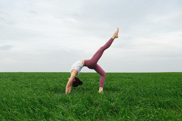 Jong slank meisje doet yoga buiten in een groen veld