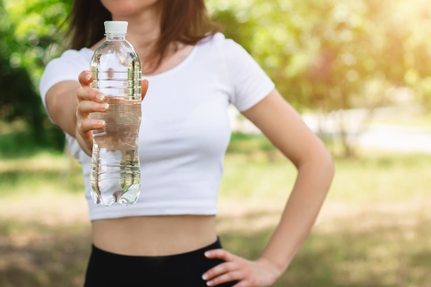 Jong slank meisje in een wit T-shirt met een fles mineraalwater.