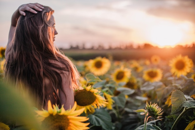 Jong slank meisje topless poseert bij zonsondergang in een veld met zonnebloemen