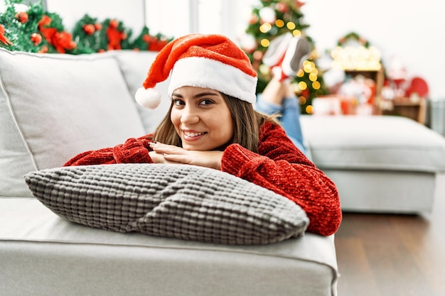 Jong spaans meisje glimlachend gelukkig liggend op de bank bij de kerstboom thuis.