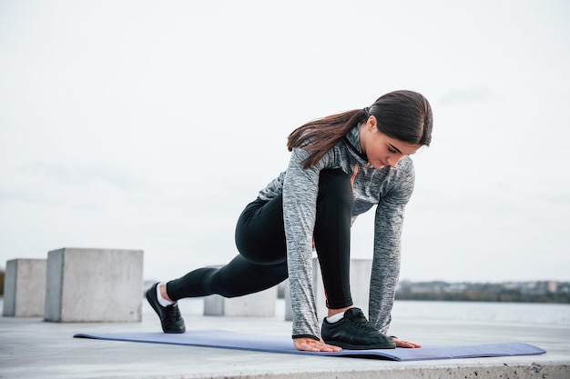 Jong sportief meisje doet yoga-oefeningen op fitnessmat buiten in de buurt van het meer overdag