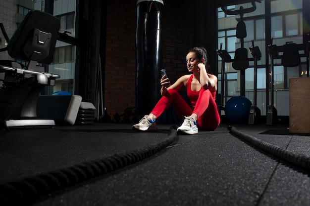 Jong sportief meisje in rode sportkleding gebruikt smartphone in de sportschool en glimlacht