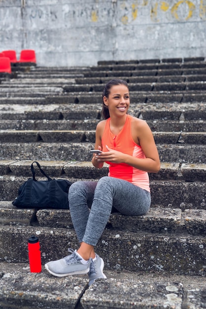 Jong sportief meisje sms't op een mobiele telefoon tijdens het trainen