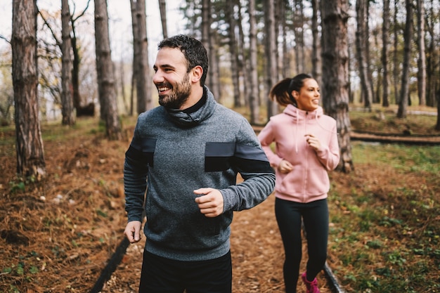 Jong sportief vrolijk paar dat in bos loopt en voor marathon voorbereidingen treft. de man is sneller dan de vrouw en hij wint.