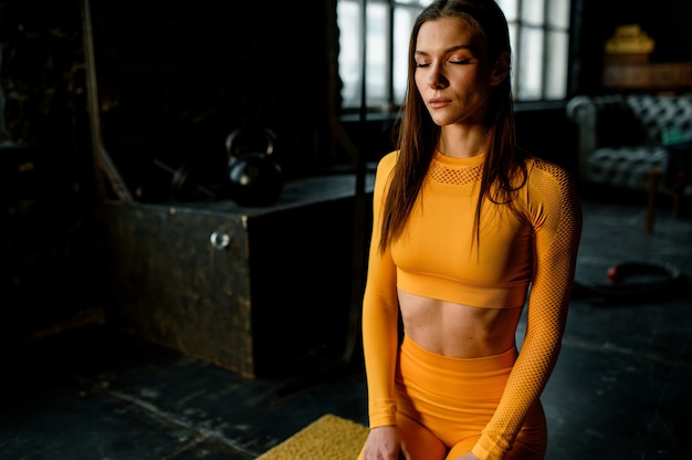 Jong sportmeisje in een geel sportuniform maak je klaar voor een training. Moderne fitnessruimte in loftstijl.