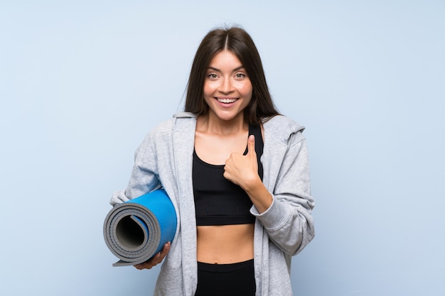 Jong sportmeisje met mat over geïsoleerde blauwe muur met verrassingsgelaatsuitdrukking