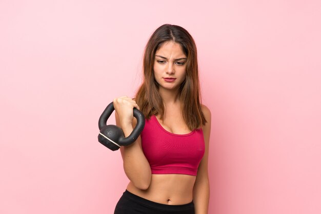 Jong sportmeisje over geïsoleerde roze muur die gewichtheffen met kettlebell maken
