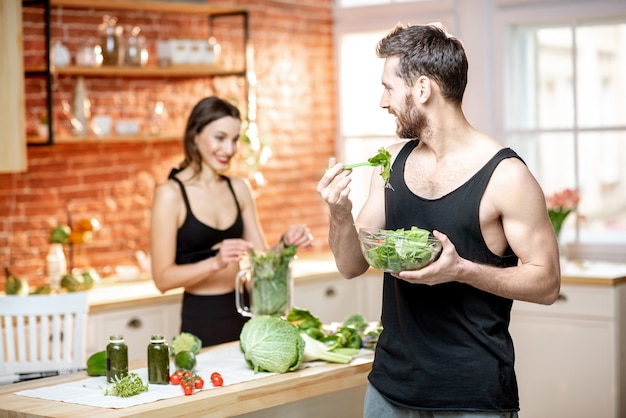 Jong sportpaar met snack met gezonde salade en groene smoothie in de keuken thuis
