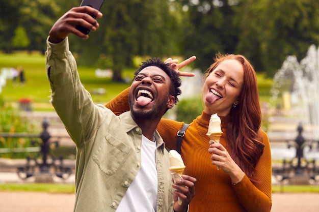 Jong stel dat samen door de stad reist en ijsjes eet in het park en een selfie neemt